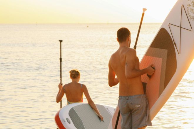 A couple enjoys paddleboarding at sunset on a serene Barcelona beach, capturing leisure and adventure.